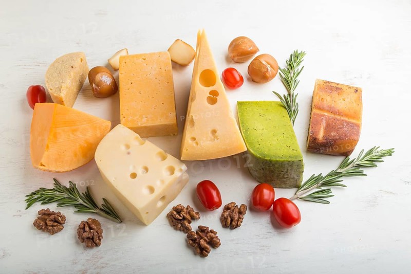 Set of different types of cheese with rosemary and tomatoes on a white wooden background. Side view, close up