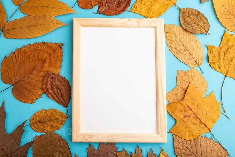 Composition with yellow and brown autumn leaves and wooden frame mockup on blue pastel background. Blank, flat lay, top view, still life, copy space