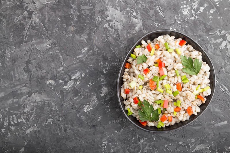 Pearl barley porridge with vegetables in blue ceramic bowl on a black concrete background. Top view, flat lay, copy space. Russian traditional cuisine