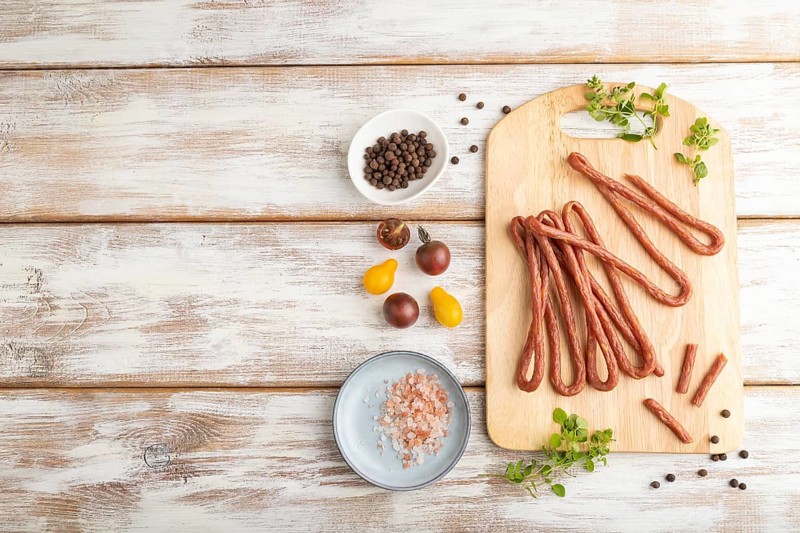 Traditional polish smoked pork sausage kabanos on cutting board with salt and pepper on white wooden background. Top view, flat lay, copy space