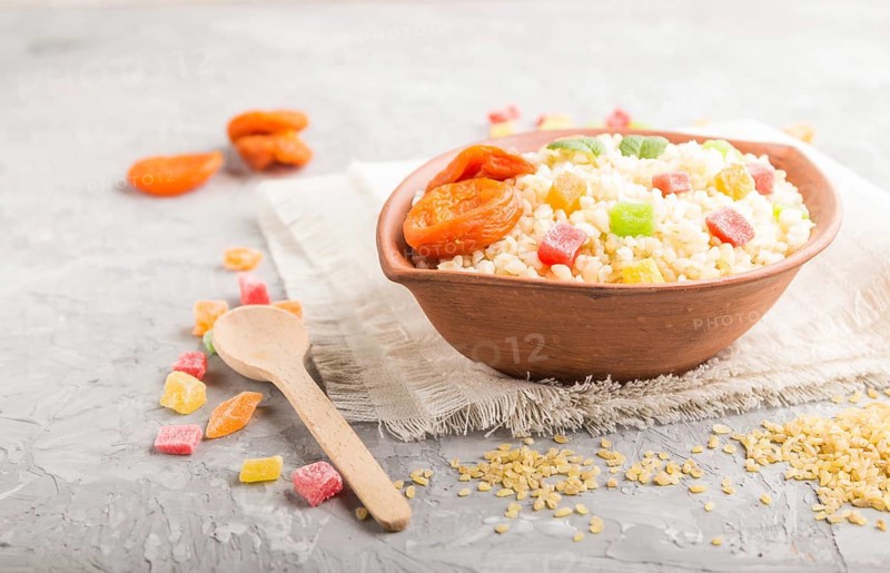 Bulgur porridge with dried apricots and candied fruits in clay bowl on a gray concrete background and linen textile. Side view, close up, selective focus. Turkish traditional cuisine