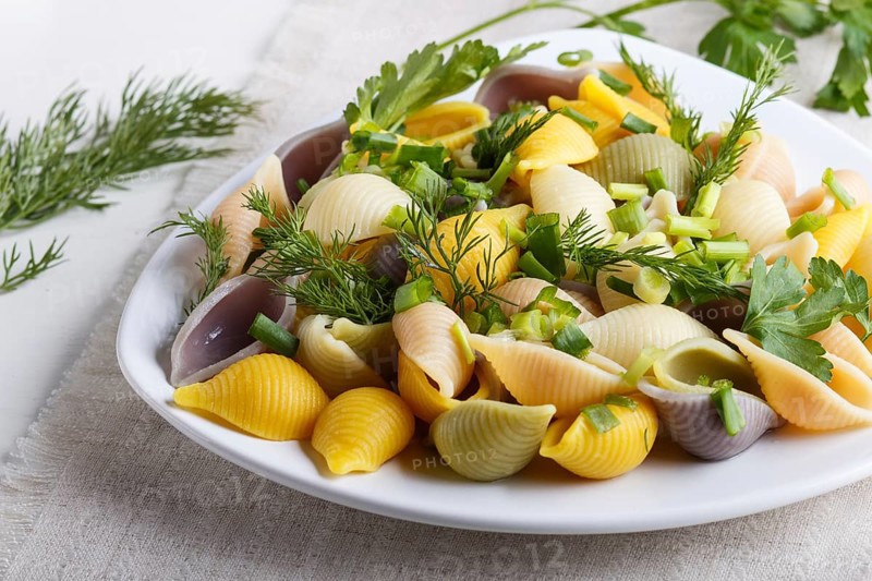Conchiglie colored pasta with fresh greengrocery on a linen tablecloth on white wooden background. close up, selective focus