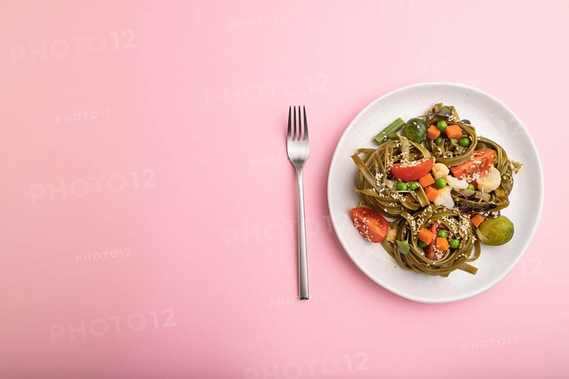 Tagliatelle green spinach pasta with tomato, pea and microgreen sprouts on a pastel pink background. Top view, flat lay, copy space