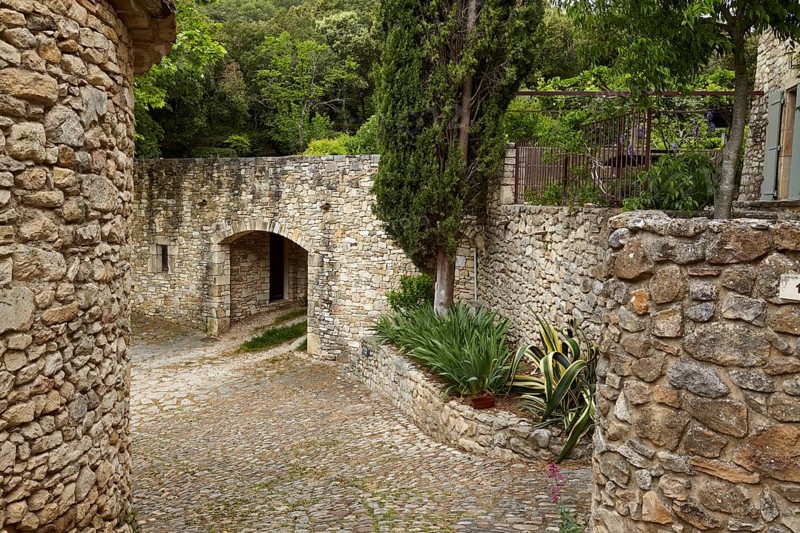Paths and walls made of natural stone with an archway and Mediterranean gardens in La Roque-sur-Cèze, Département Gard, Occitanie region, France, Europe