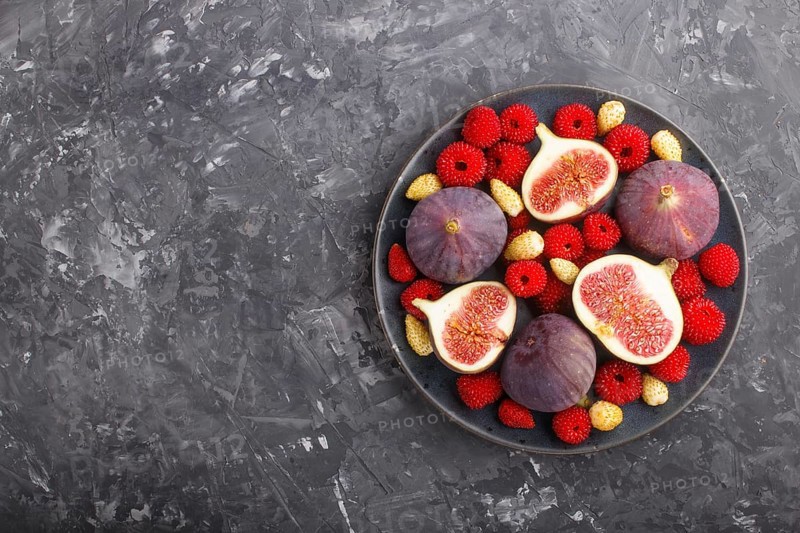 Fresh figs, strawberries and raspberries on blue ceramic plate on black concrete background. top view, flat lay, copy space