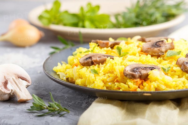 Yellow fried rice with champignons mushrooms, turmeric and oregano on blue ceramic plate on a gray concrete background and yellow textile. side view, close up, selective focus