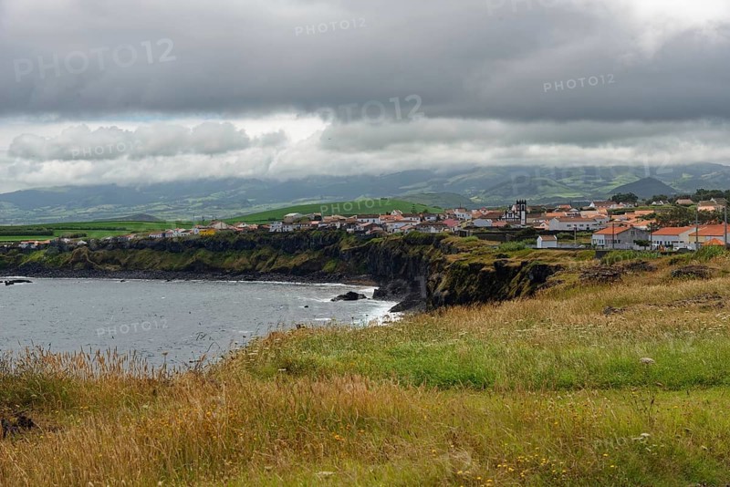 A village on the coast with green cliffs and a cloudy sky, Fenais da Luz, Sao Miguel Island, Azores, Portugal, Europe