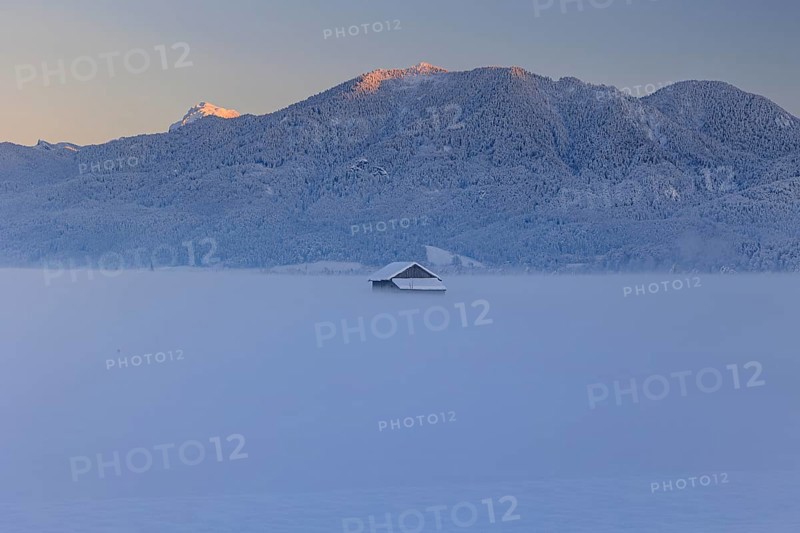 Hut in the snow in front of mountains, evening light, view of Rabenkopf and Benediktenwand, Schlehdorf, Alpine foothills, Upper Bavaria, Bavaria, Germany, Europe