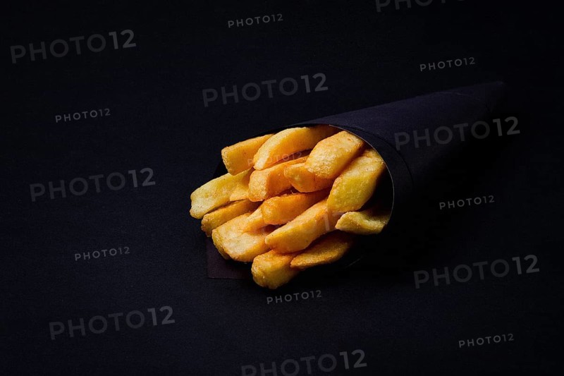French fries, in black paper packaging, on a black background, close-up, selective focus