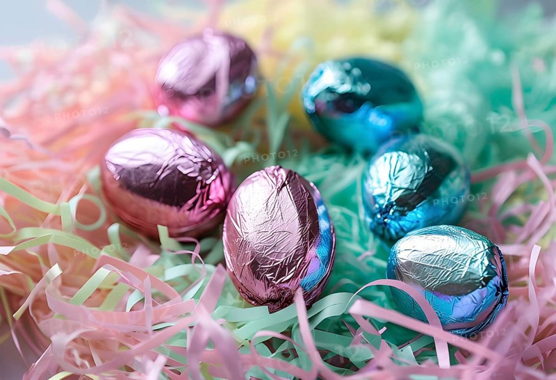 Small chocolate Easter eggs wrapped in shiny foil, placed on a bed of shredded pastel-colored paper, AI generated