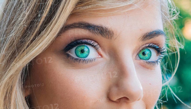 Close-up of a female face with blonde hair and intense green eyes, natural background, AI generated, AI generated