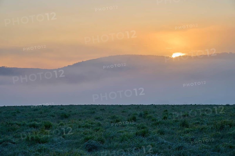 Sunset behind fog-covered hills with a green meadow in the foreground, Mönchberg, Miltenberg, Spessart, Bavaria, Germany, Europe