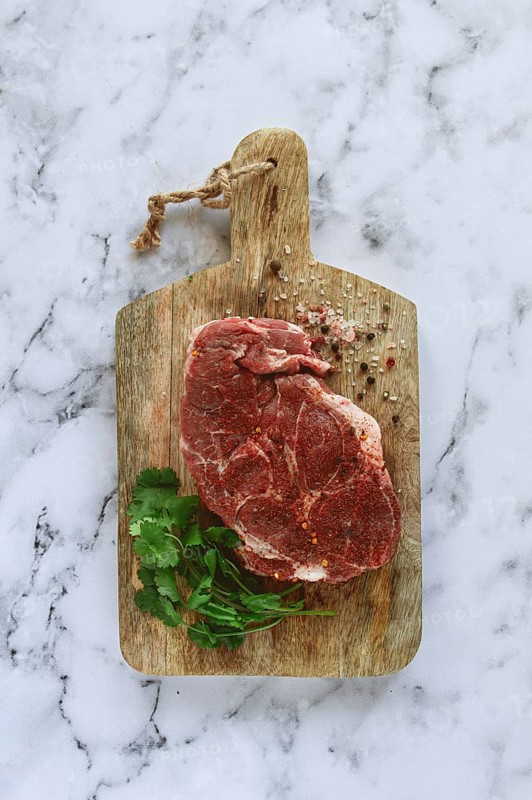 Raw pork steak, pork neck, on a chopping board, marble table, top view, with spices and coriander, no people