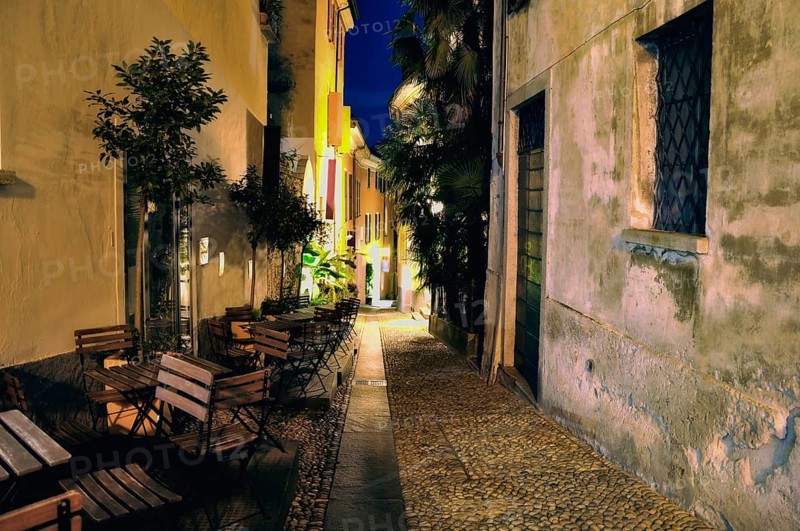 Old Narrow Alley Illuminated at Night with Chairs and Tables in City of Locarno, Ticino, Switzerland, Europe