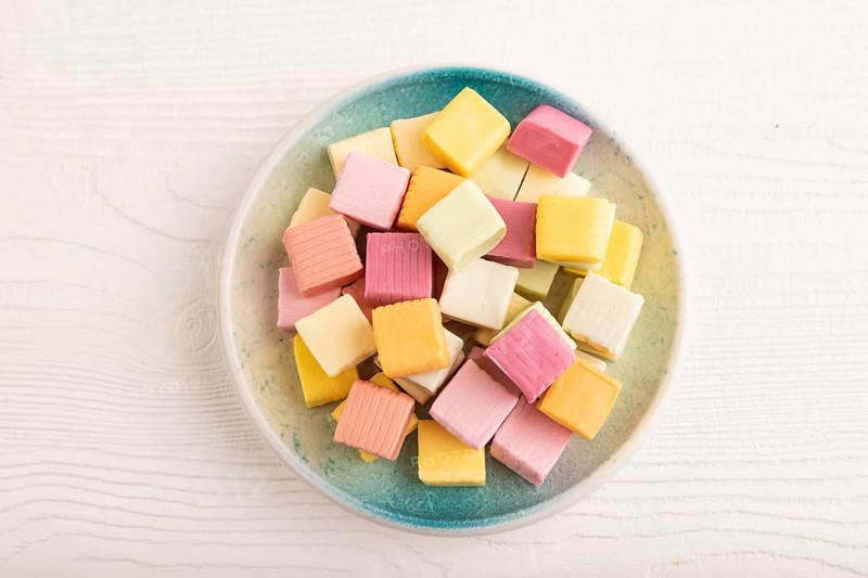 Various fruit jelly chewing candies on plate on white wooden background. apple, banana, tangerine, kiwi, top view, flat lay, close up