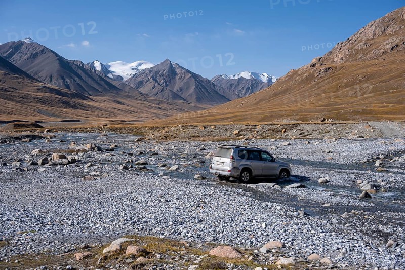 Off-road vehicle crossing a river in the Burkhan valley, mountain landscape with glaciated peaks and golden meadows, Terskey Ala-Too, Tien Shan, Issyk Kul province, Kyrgyzstan, Asia