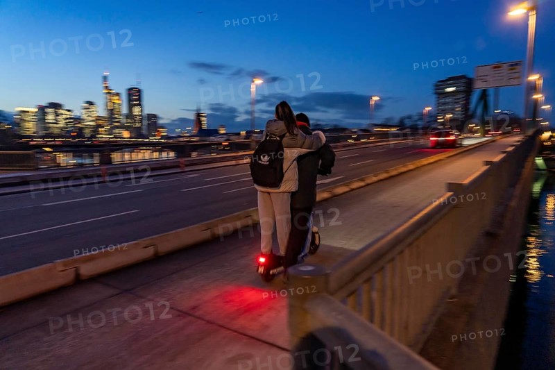 Skyline of the city centre of Frankfurt am Main, e-scooter, 2 persons, on the raft bridge, dusk, river Main, winter, Hesse, Germany, Europe