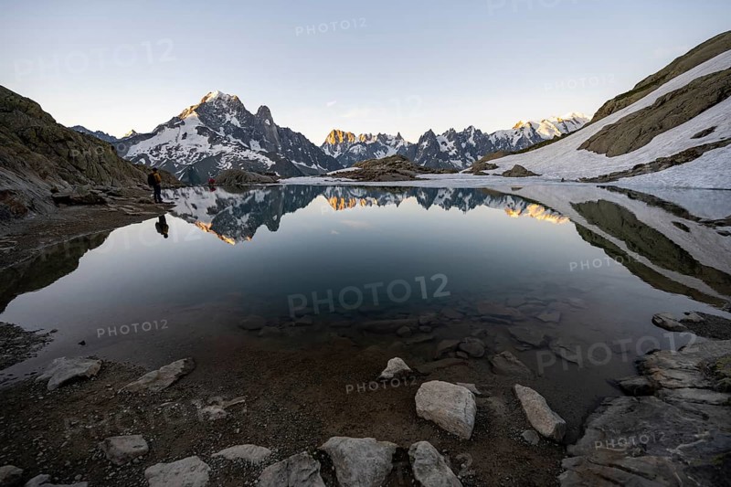 Tourist at a mountain lake in the morning, mountain landscape at sunrise, water reflection in Lac Blanc, mountain peak, Aiguille Verte, Grandes Jorasses, Aiguille du Moine, Mont Blanc, Mont Blanc massif, Chamonix-Mont-Blanc, Haute-Savoie, France, Europe