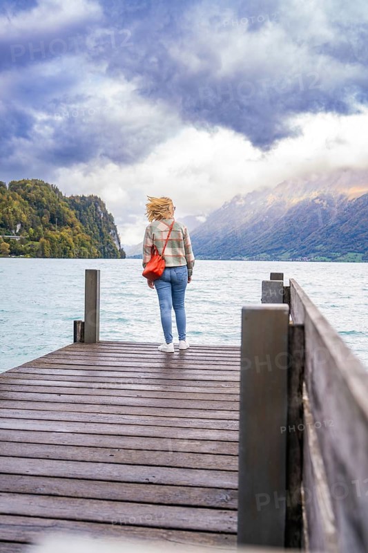 Person standing on a wooden footbridge with a view of the lake and mountains under a cloudy sky, Lake Brienz, Switzerland, Europe