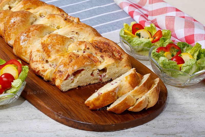 Swabian cuisine, hearty yeast plait with smoked meat, salty wreath bread, yeast yeast dough pastry, arranged on wooden board, baked, grandmother's kitchen, regional, home cooking, typical Swabian reinterpreted, traditional cuisine reinterpreted, salad in the back, small bowl, food photography, studio, Germany, Europe