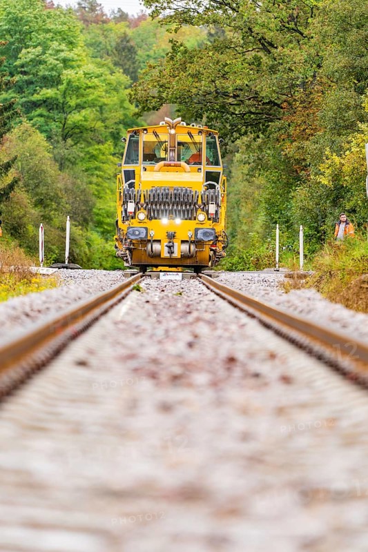 A yellow tractor unit drives directly towards the viewer, surrounded by autumnal forest, Hermann Hesse Bahn track construction, Calw district, Black Forest, Germany, Europe