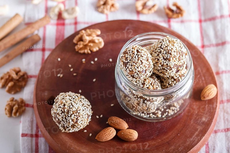 Energy balls cakes with almonds, sesame, cashew, walnuts, dates and germinated wheat on wooden board in glass jar, side view, close up