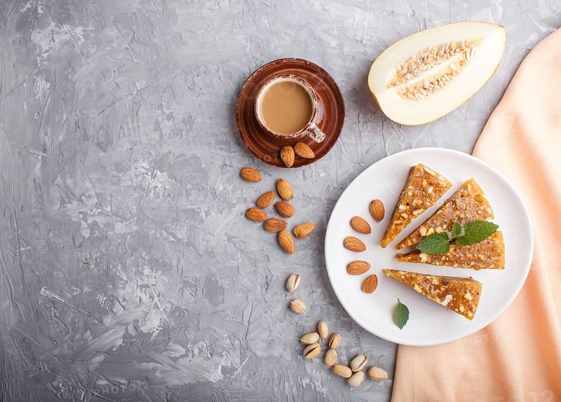 Traditional turkish candy cezerye made from caramelised melon, roasted walnuts, hazelnuts, cashew, pistachios on white ceramic plate and a cup of coffee on a gray concrete background. top view, flat lay, copy space