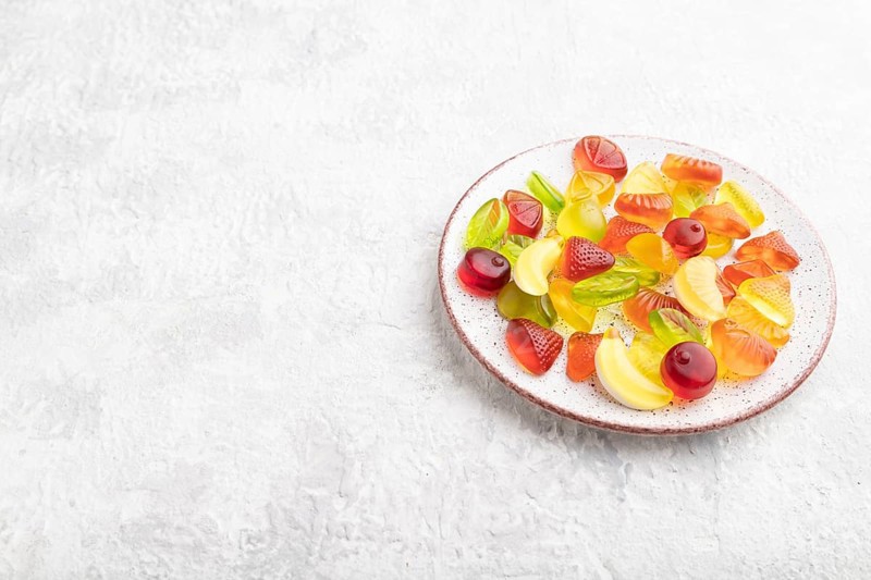 Various fruit jelly candies on plate on gray concrete background. side view, copy space