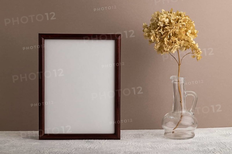 Brown wooden frame mockup with dried hydrangea in glass on beige paper background. Blank, vertical orientation, still life, copy space