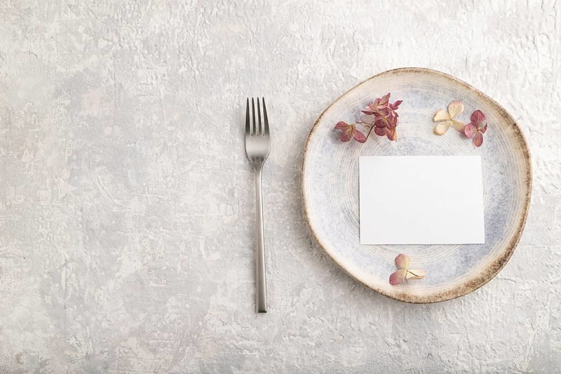 White paper invitation card, mockup with dried hydrangea flowers on ceramic plate and gray concrete background. Blank, flat lay, top view, still life, copy space