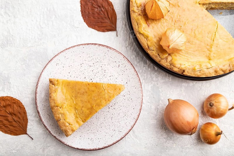 Autumn onion pie decorated with leaves and cup of coffee on gray concrete background. Top view, flat lay, close up