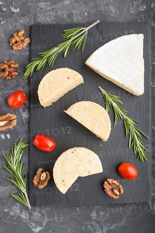 Cheddar cheese and various types of cheese with rosemary and tomatoes on black slate board on a black concrete background. Top view, close up, copy space