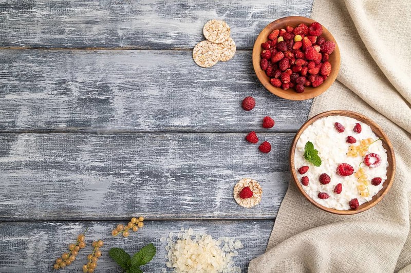 Rice flakes porridge with milk and strawberry in wooden bowl on gray wooden background and linen textile. Top view, flat lay, copy space