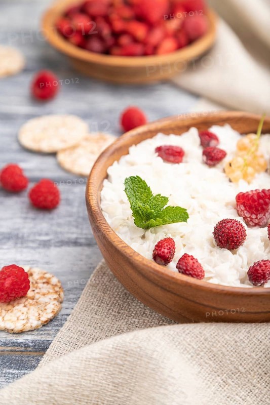 Rice flakes porridge with milk and strawberry in wooden bowl on gray wooden background and linen textile. Side view, selective focus, close up