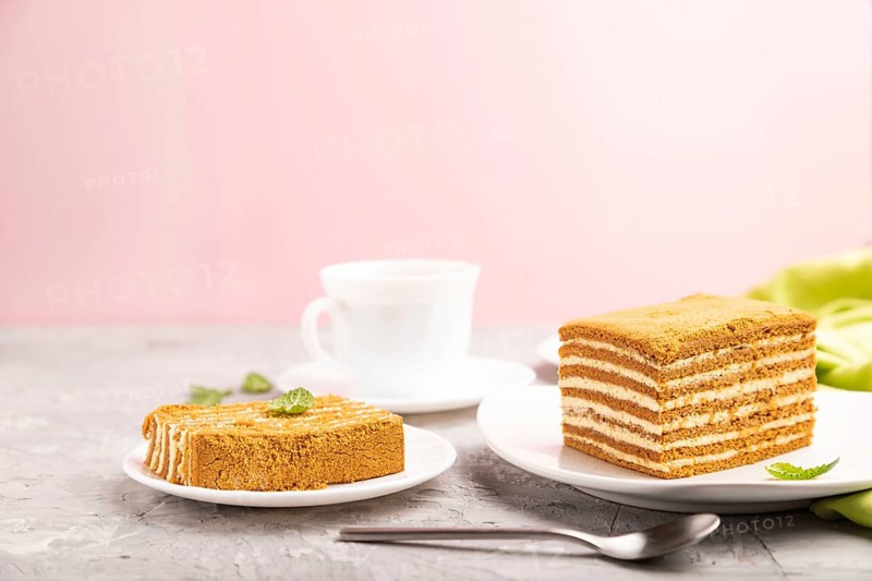 Homemade honey cake with milk cream and mint with cup of coffee on a and pink background and green textile. Side view, copy space, selective focus