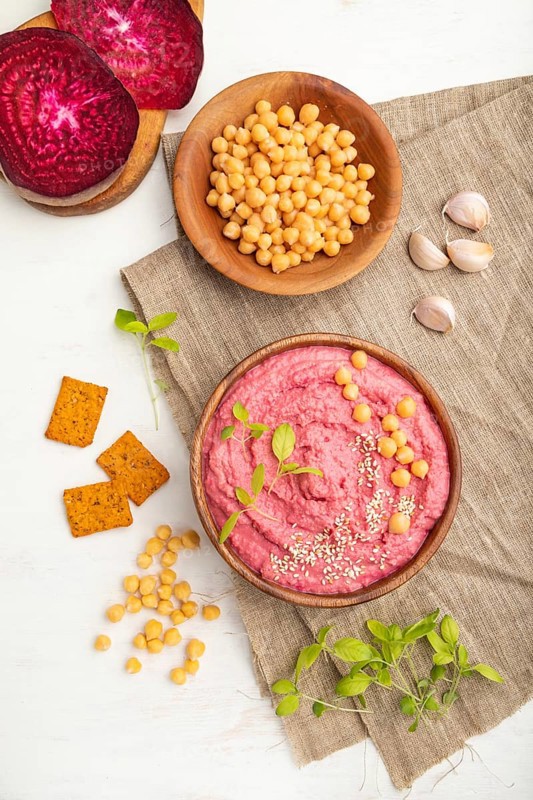 Hummus with beet and microgreen basil sprouts in wooden bowl on a white wooden background and linen textile. Top view, flat lay, close up