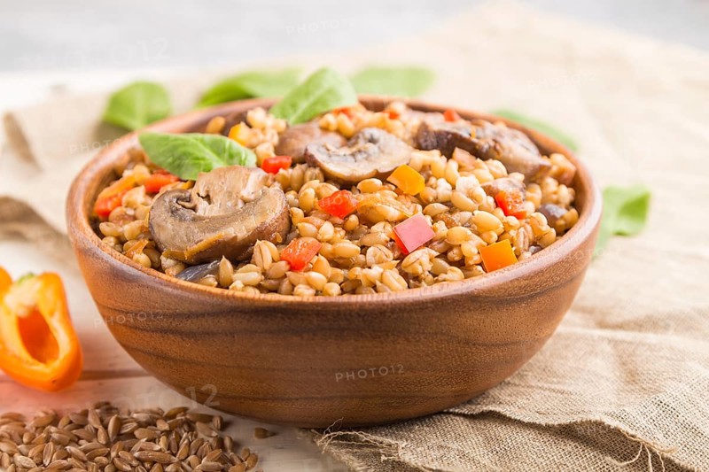 Spelt (dinkel wheat) porridge with vegetables and mushrooms in wooden bowl on a white wooden background and linen textile. Side view, selective focus. Russian traditional cuisine