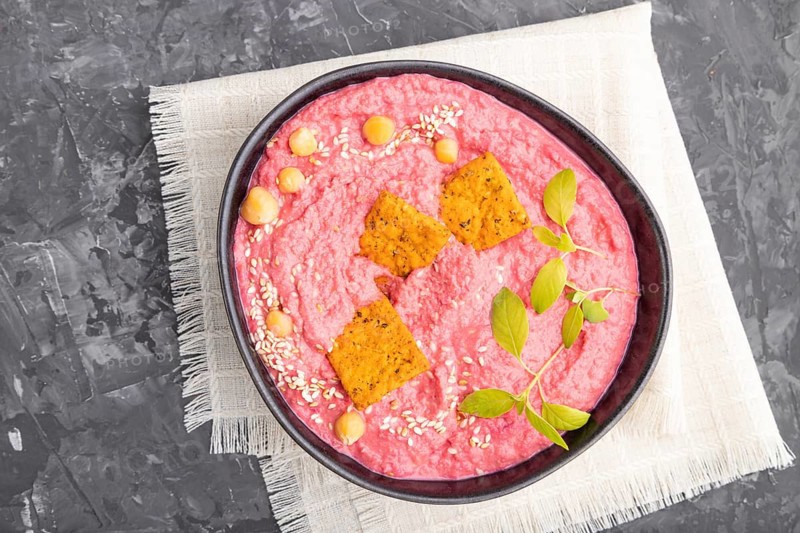 Hummus with beet and microgreen basil sprouts in ceramic bowl on a black concrete background and linen textile. Top view, flat lay, close up