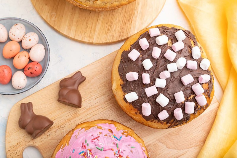 Homemade glazed and decorated easter pies with chocolate eggs and rabbits on a white concrete background and yellow textile. top view, flat lay, close up