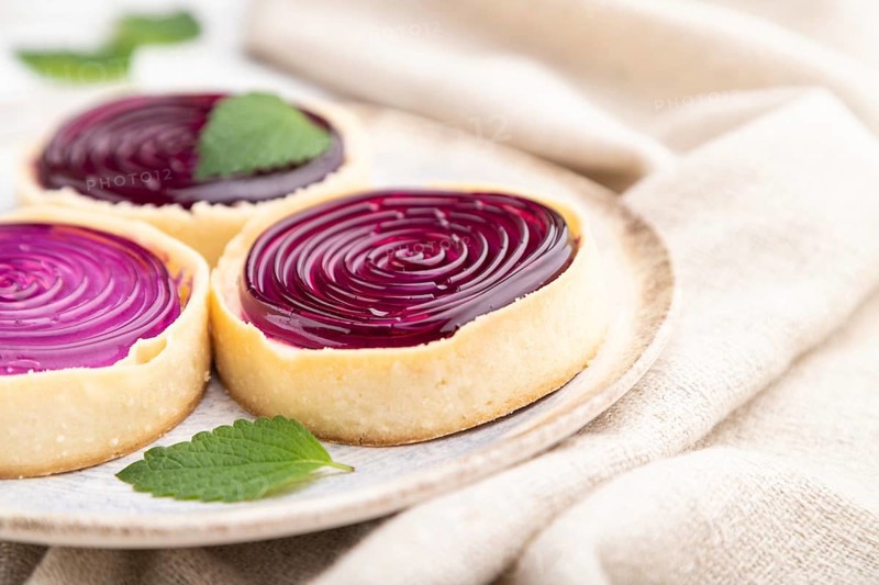 Sweet tartlets with jelly and milk cream with cup of coffee on a white wooden background and linen textile. Side view, close up, selective focus