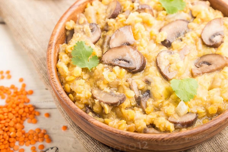 Lentils porridge with champignons and coriander in a wooden bowl on a white wooden background and linen textile. Side view, close up, selective focus