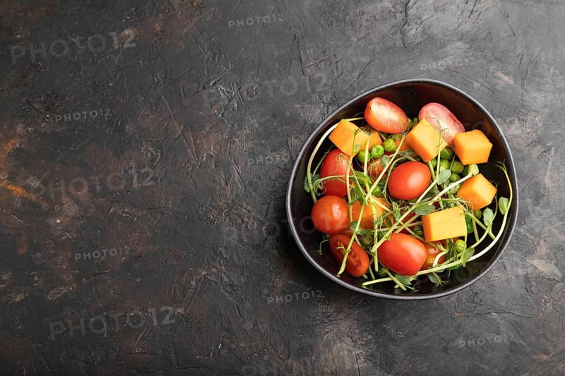 Vegetarian vegetable salad of tomatoes, pumpkin, microgreen pea sprouts on black concrete background. Top view, flat lay, copy space
