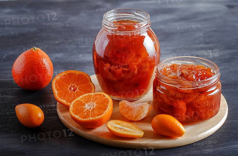Tangerine and kumquat jam in a glass jar with fresh fruits on a black wooden table. Homemade, copy space, close up