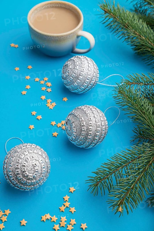 Christmas or New Year composition. Decorations, silver balls, fir and spruce branches, cup of coffee, on a blue paper background. Side view, colose up