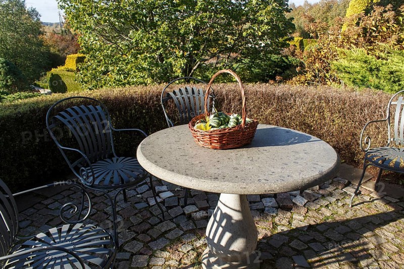 Garden furniture, stone table with a basket with decorative pumpkins. Modern landscape design with topiary and hedges on background