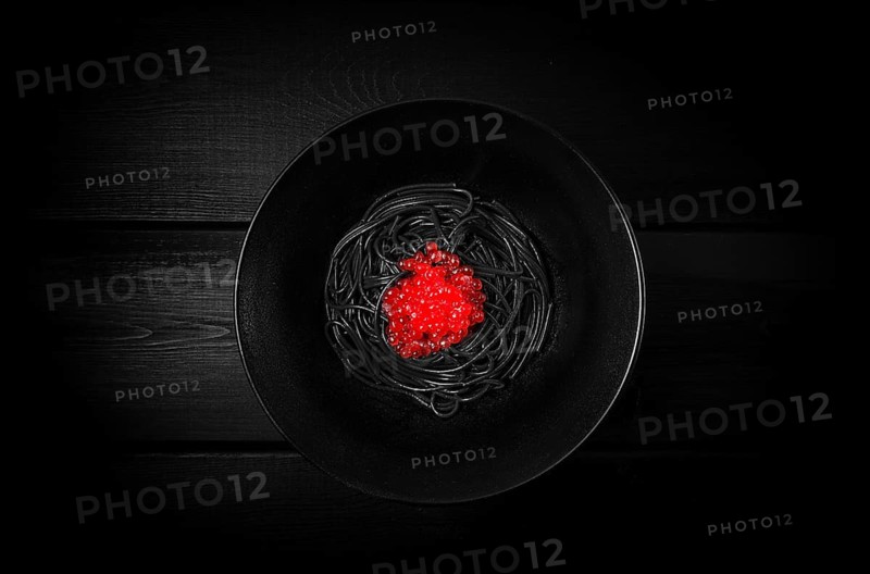 Black spaghetti with red caviar, pasta, on a black background, top view, no people