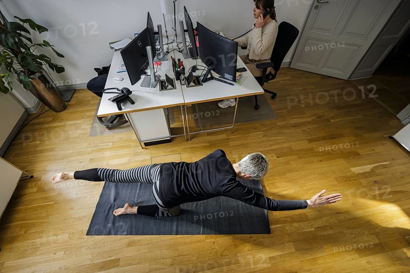 Symbolic photo on the subject of occupational health management. A woman exercises on a sports mat in front of her desk during her office break. Berlin, 13.02.2024