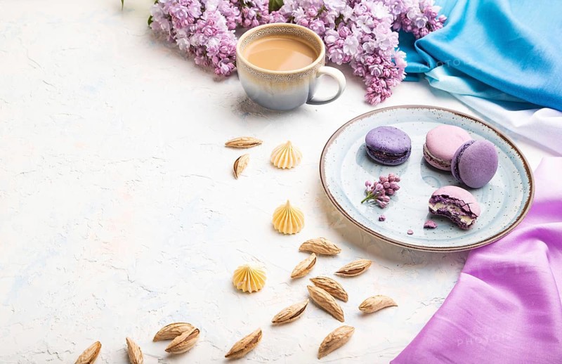 Purple macarons or macaroons cakes with cup of coffee on a white concrete background and magenta-blue textile. Side view, copy space