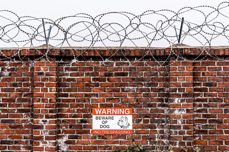 Company premises, wall secured with rolls of barbed wire, signpost for guard dog on the premises