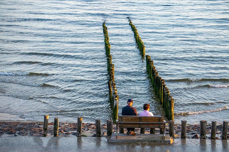 An elderly couple sitting on a bench on the beach, at high tide, breakwater, Netherlands